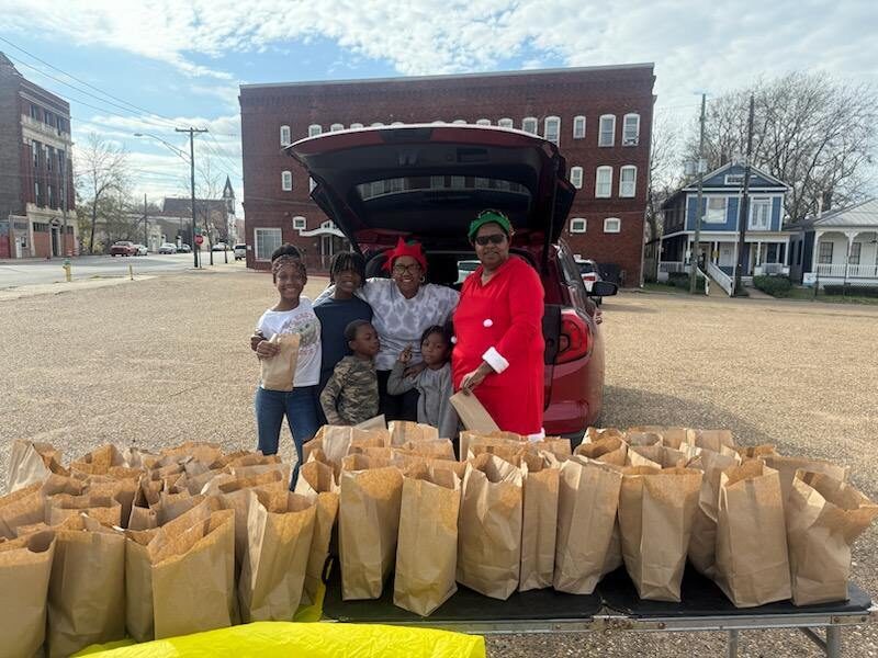Volunteers in holiday hats hand out paper bags of food from the back of a car downtown.