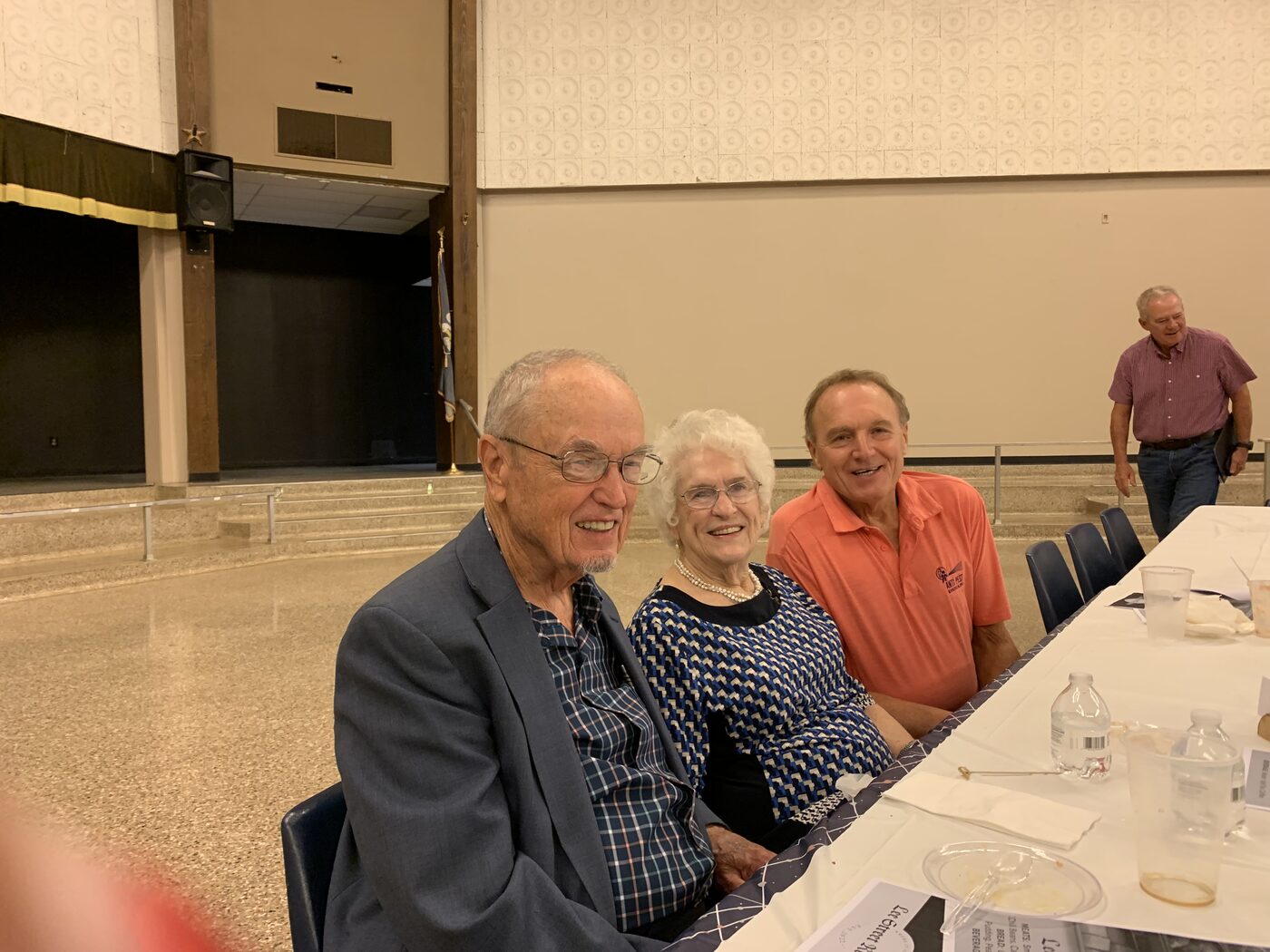 Three guests share a laugh at a banquet table inside a community hall.