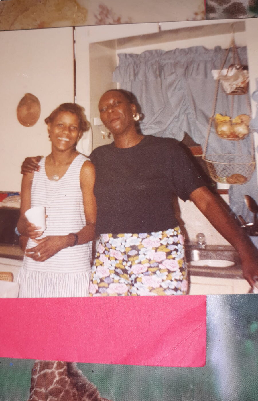 A vintage snapshot of two women posing together in a home kitchen.