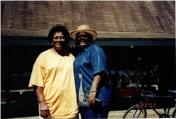 Two women smile together outside a pavilion in a sunny 2003 snapshot.
