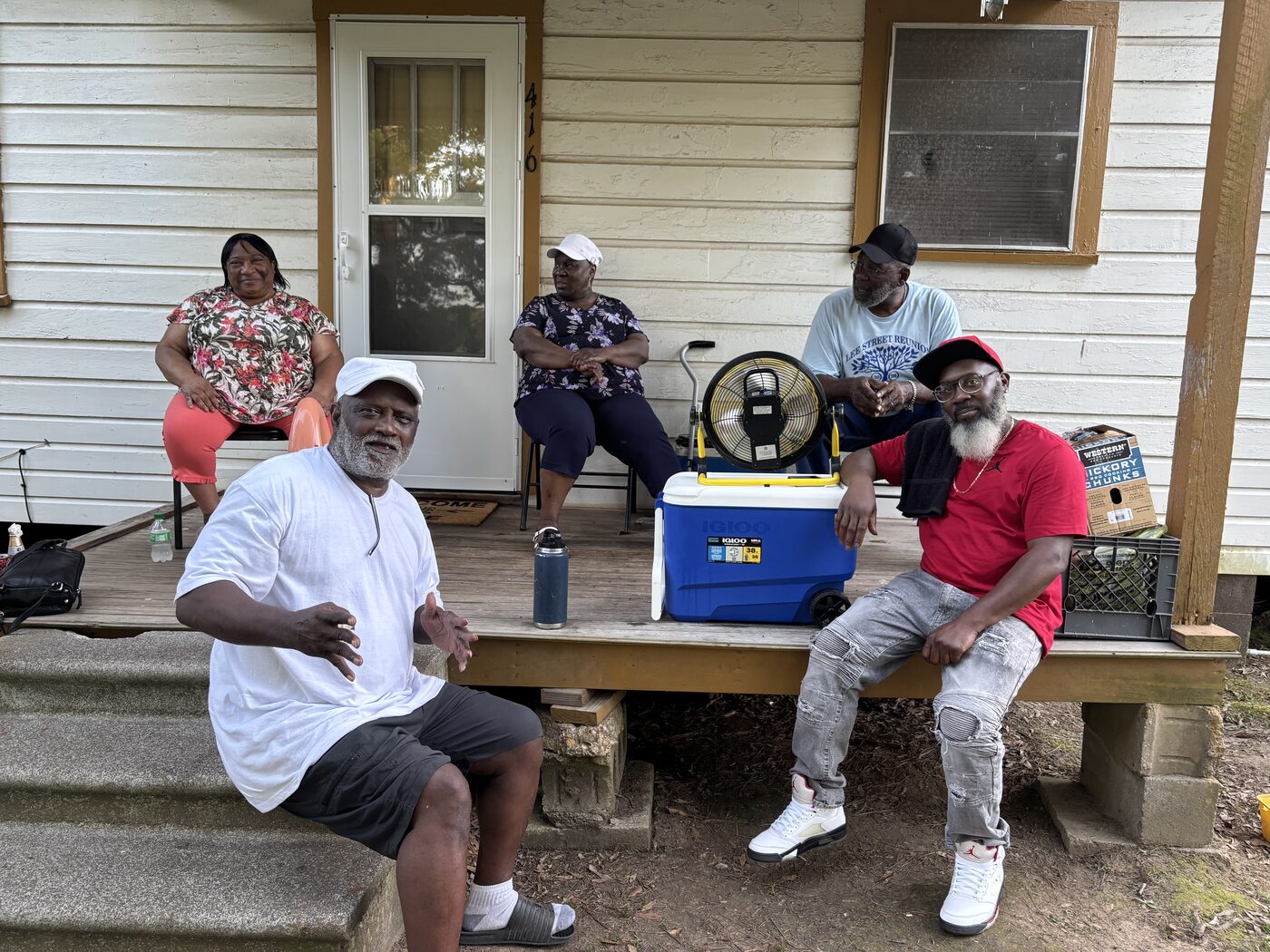 Five friends relax on a front porch during a reunion weekend, one wearing a Lee Street Reunion shirt.