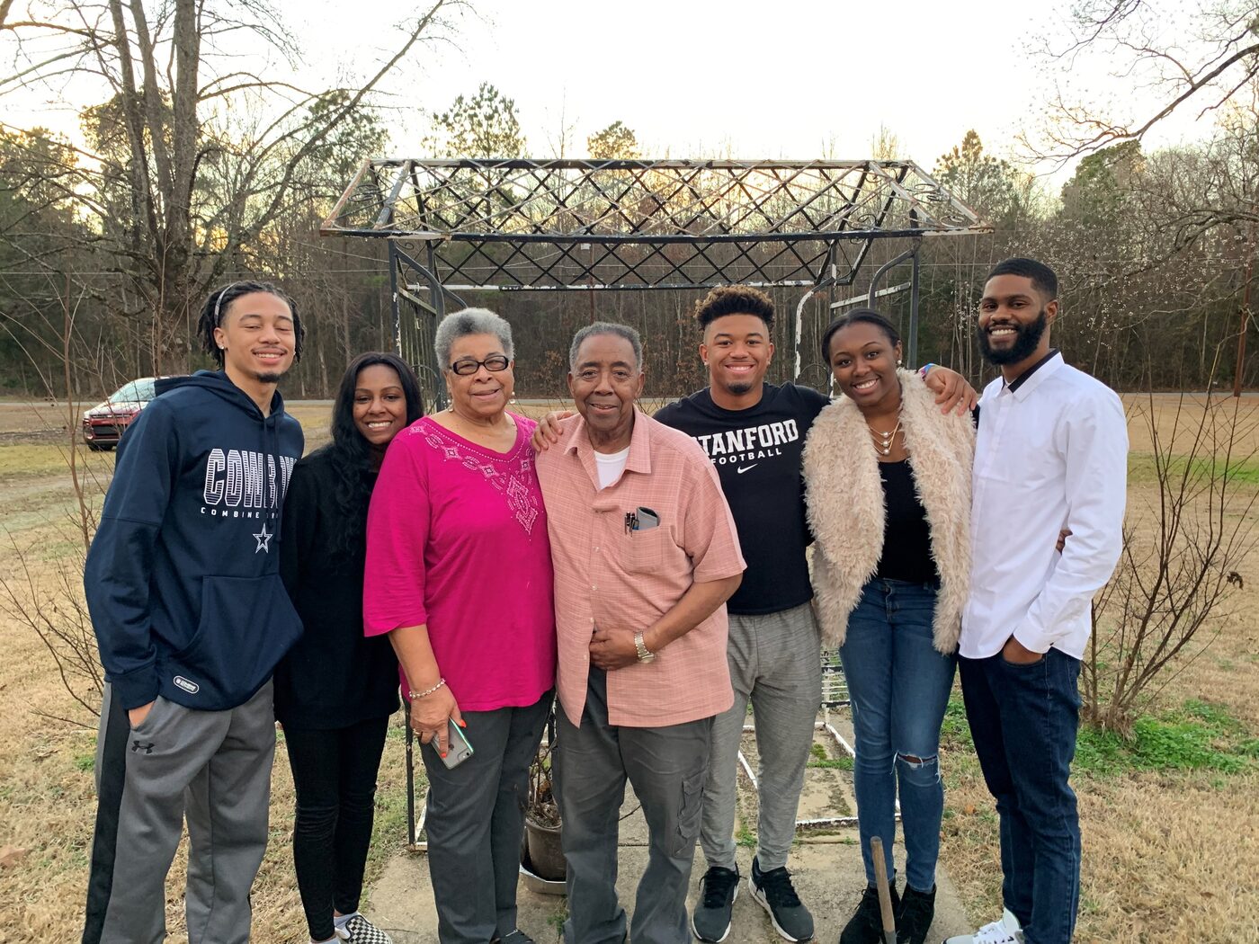 Three generations of a family gather outdoors in front of an old garden arbor.