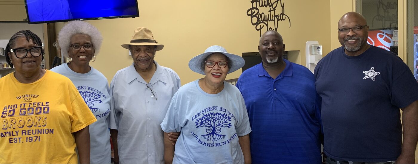 Six friends in reunion shirts smile together inside a community cafeteria.