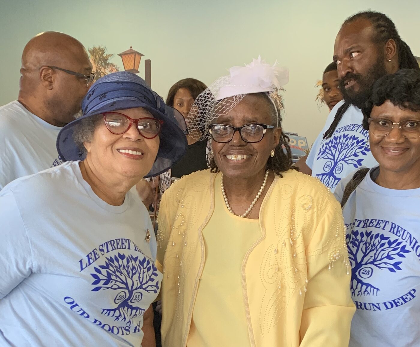 Two women in Sunday hats smile closely together at a reunion gathering.