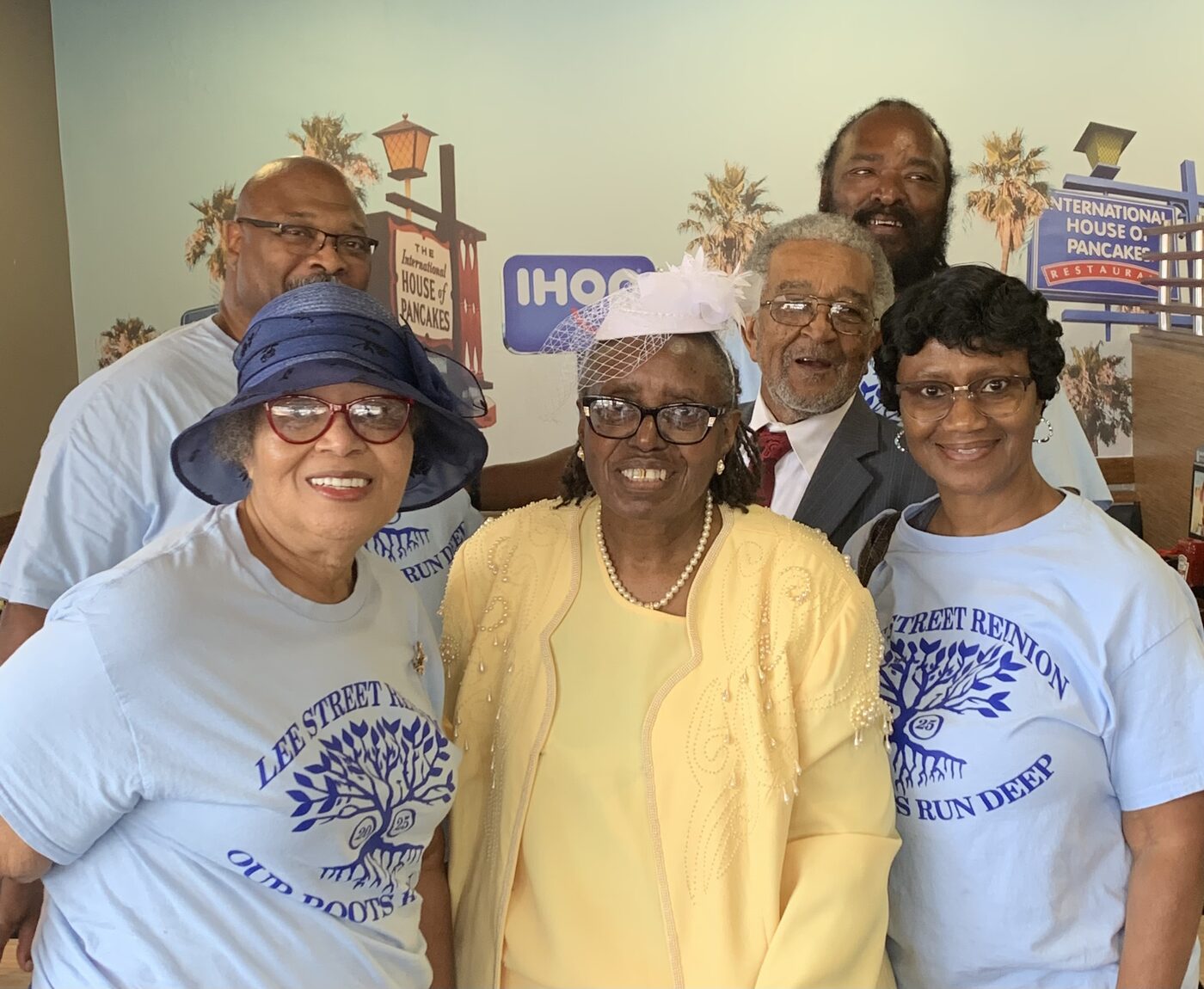 A group in matching reunion shirts poses together at a restaurant breakfast gathering.