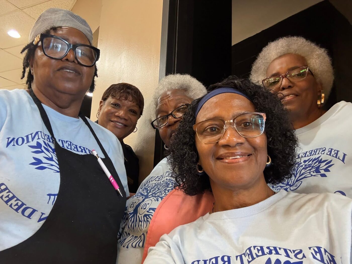 Five volunteers in reunion shirts take a cheerful group selfie.