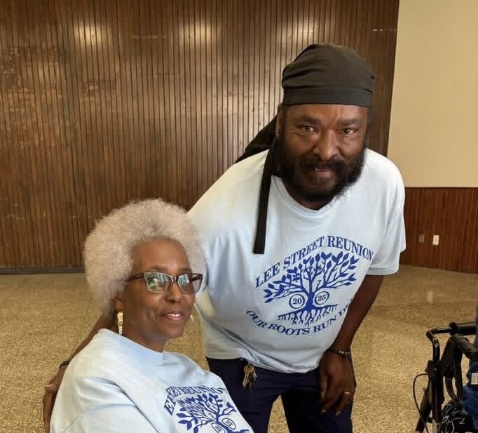 A man in a reunion shirt leans in beside a seated woman for a warm photo.