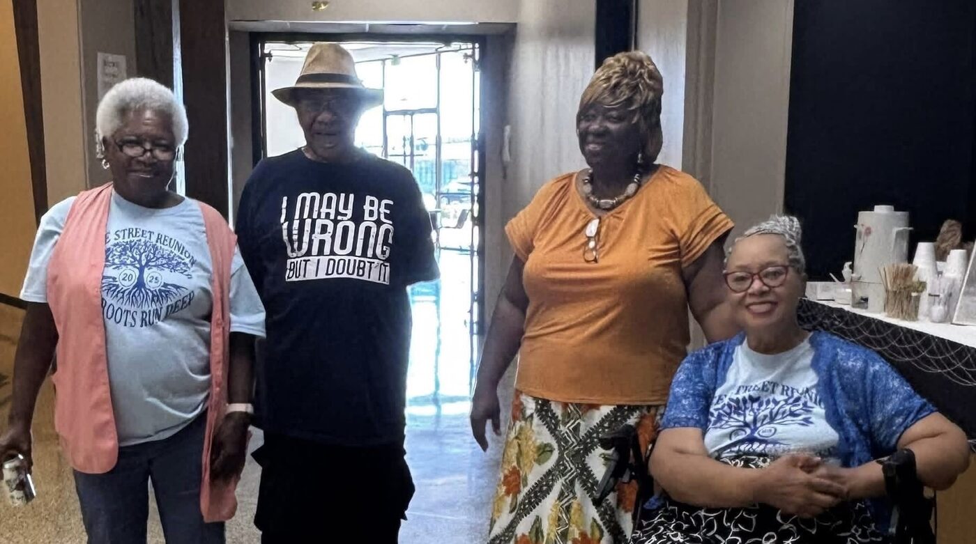 Four attendees in reunion shirts gather in a bright hallway during an indoor reunion event.