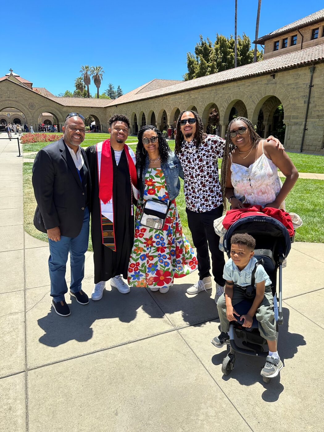 A family celebrates a graduate outside a university courtyard on a bright day.