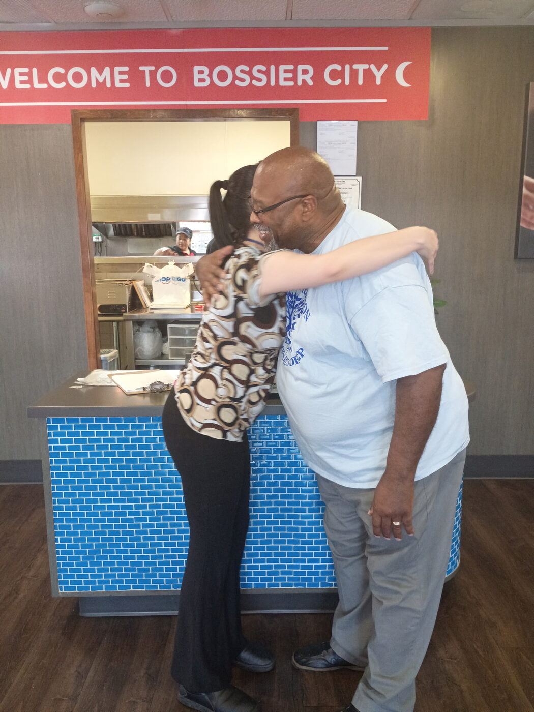 Two people share a warm hug at a restaurant counter.